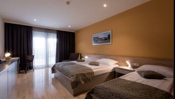 A hotel room with two beds, a desk, a chair, and a large window with curtains.