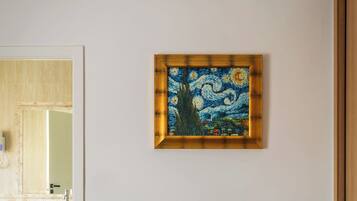 A room with a wooden desk, a chair, a painting on the wall, and a view of a bathroom.