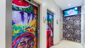 A hallway with colorful artwork on the elevator doors and a patterned wall. - Hotel Aixo Suites By Geh Suites (Cartagena)