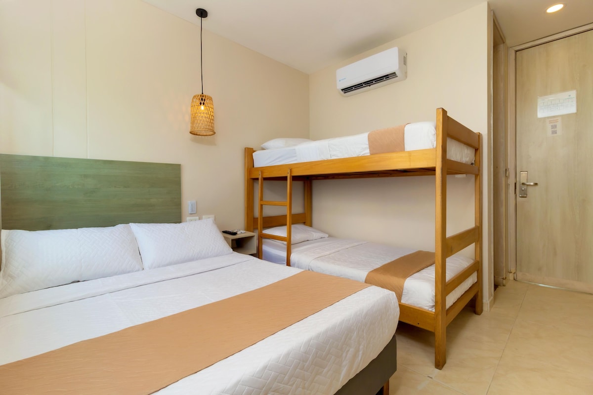 A hotel room with bunk beds, a bedside table, a lamp, and an air conditioning unit.