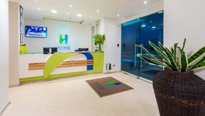 A reception area with a modern design, featuring a reception desk, a digital screen, and a glass door leading to a hallway. - Hotel Aixo Suites By Geh Suites (Cartagena)