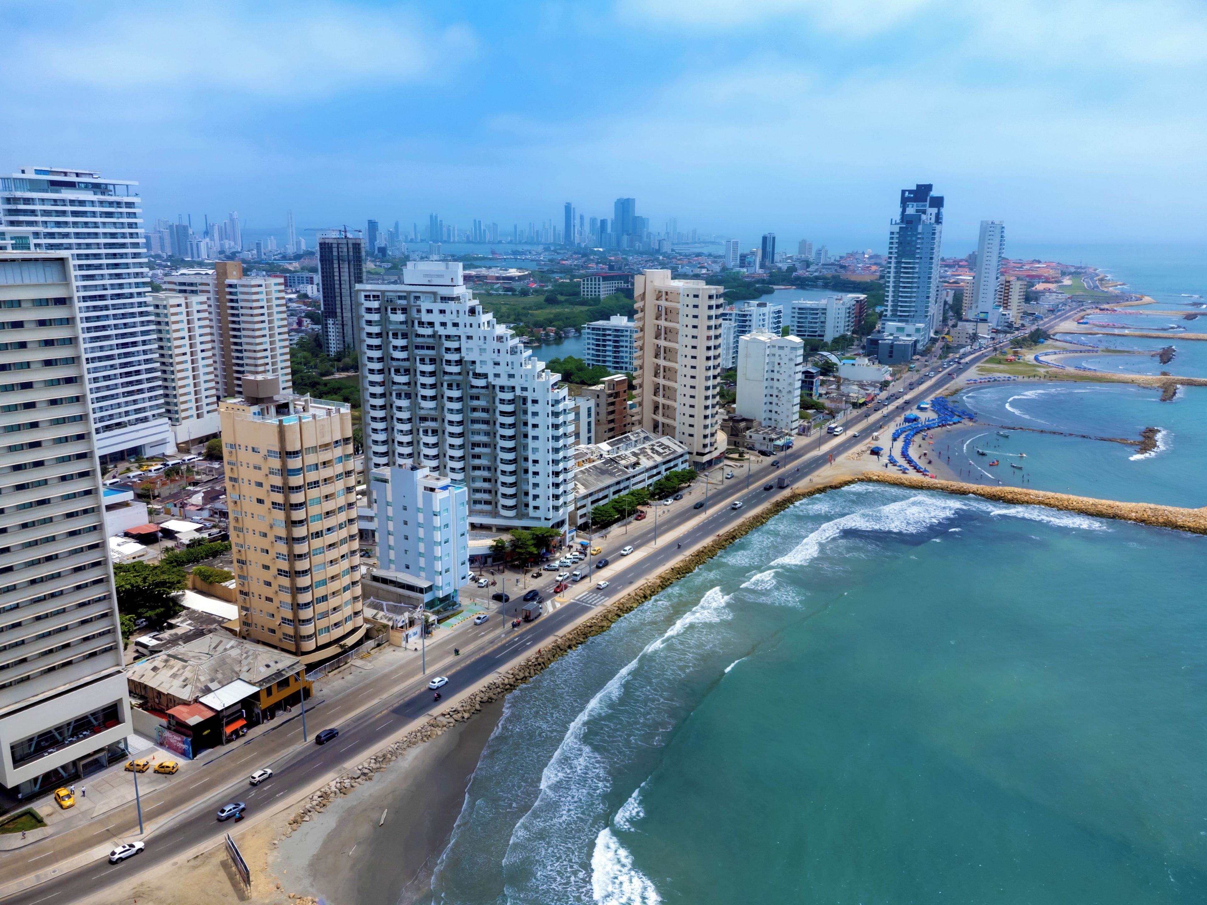 A coastal cityscape with high-rise buildings, a beach, and a road running parallel to the waterfront.