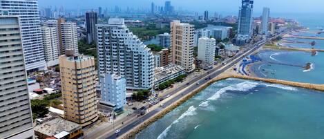 A coastal cityscape with high-rise buildings, a beach, and a road running parallel to the waterfront.