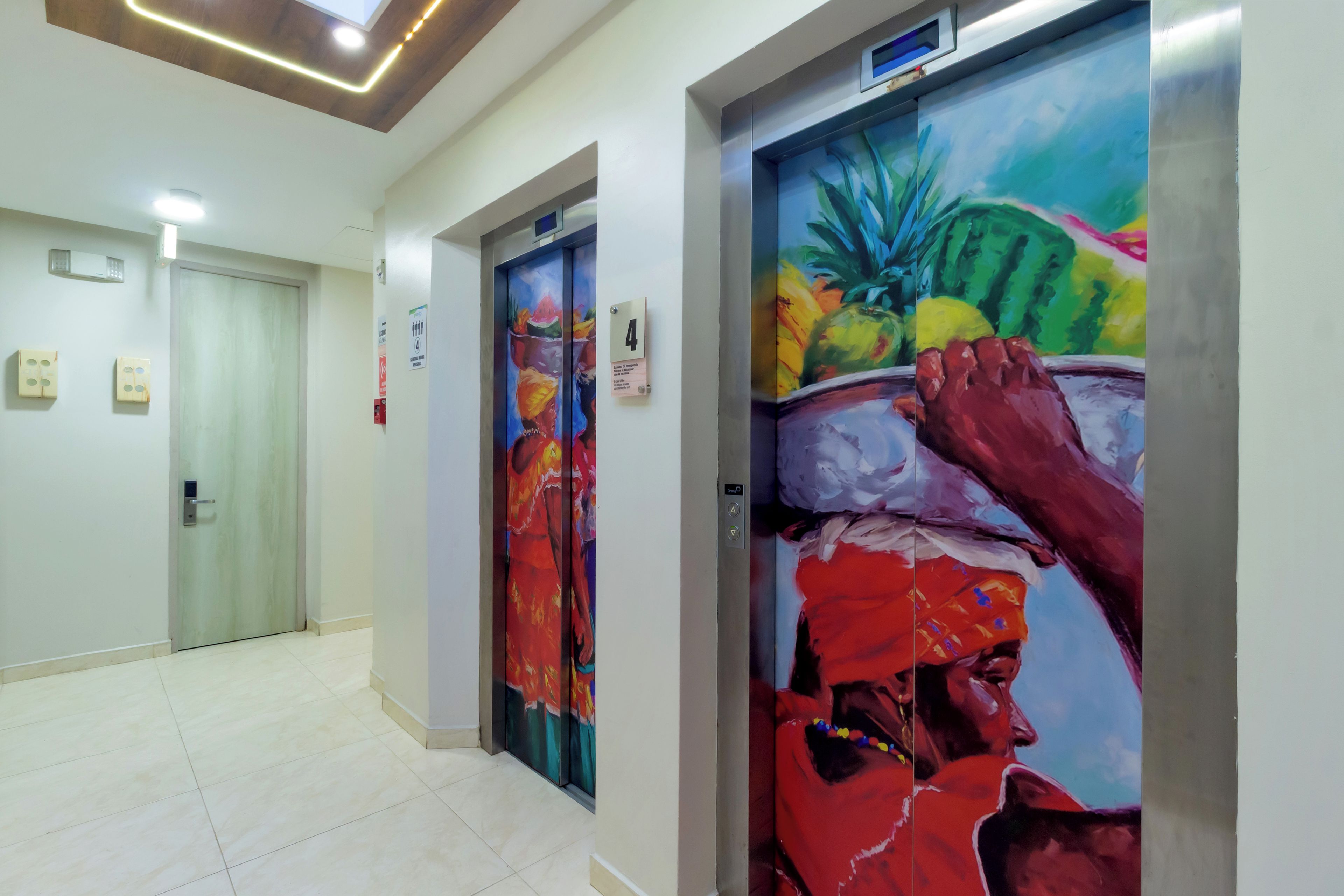 Corredor com dois elevadores, cada um com um mural colorido nas portas.