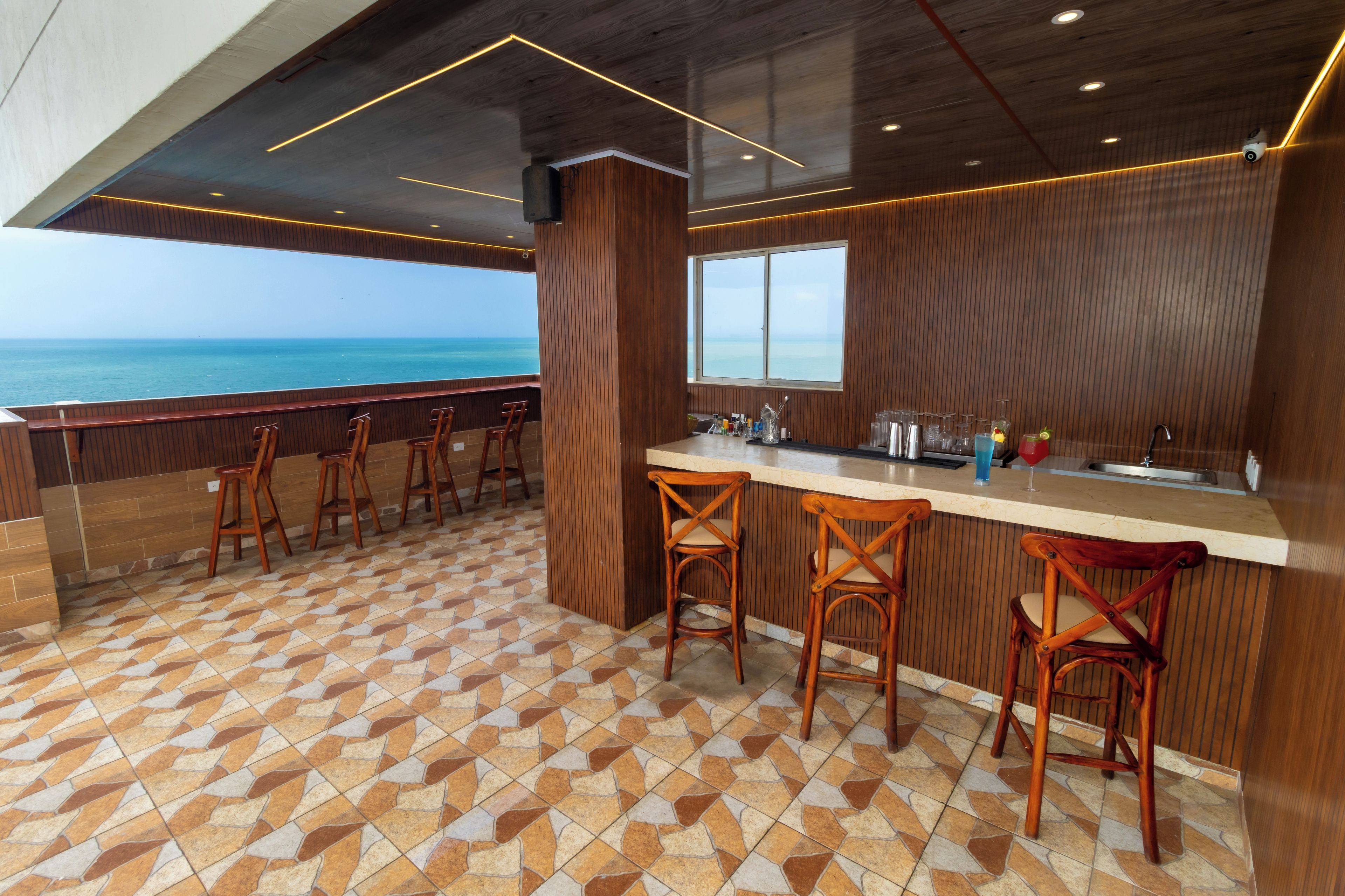 Zona de bar con vistas al mar, taburetes de madera y suelo de baldosas.