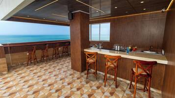 Zona de bar con vistas al mar, taburetes de madera y suelo de baldosas.
