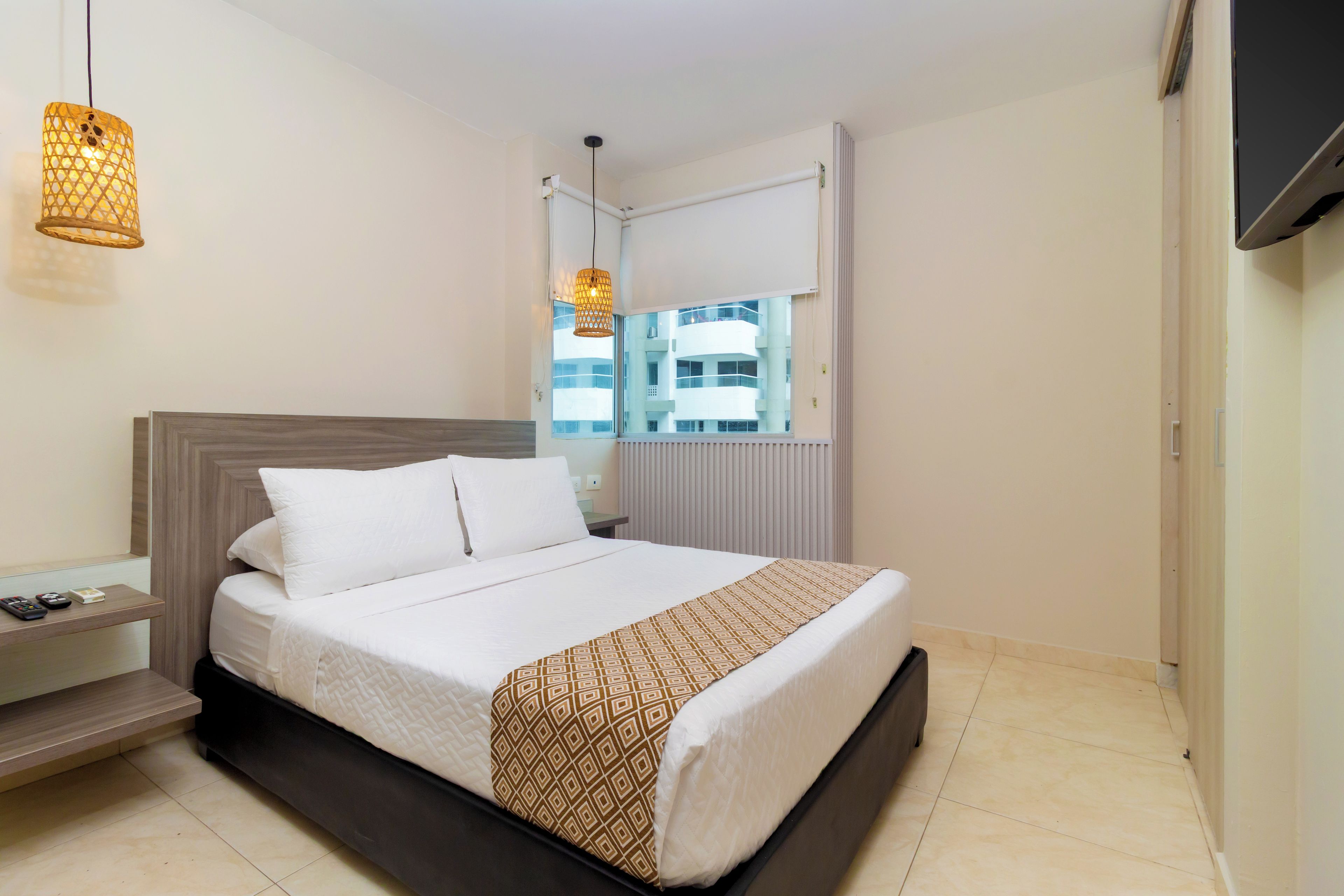 Une chambre d’hôtel avec un lit, une table de chevet, une lampe, une fenêtre et une vue sur les bâtiments environnants.