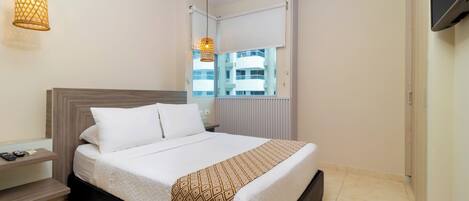 Une chambre d’hôtel avec un lit, une table de chevet, une lampe, une fenêtre et une vue sur les bâtiments environnants.