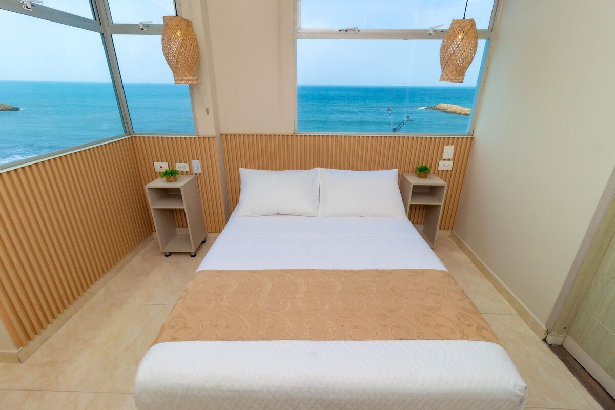 A hotel room with a large bed, wooden paneling, a view of the sea, and two bedside tables with lamps.