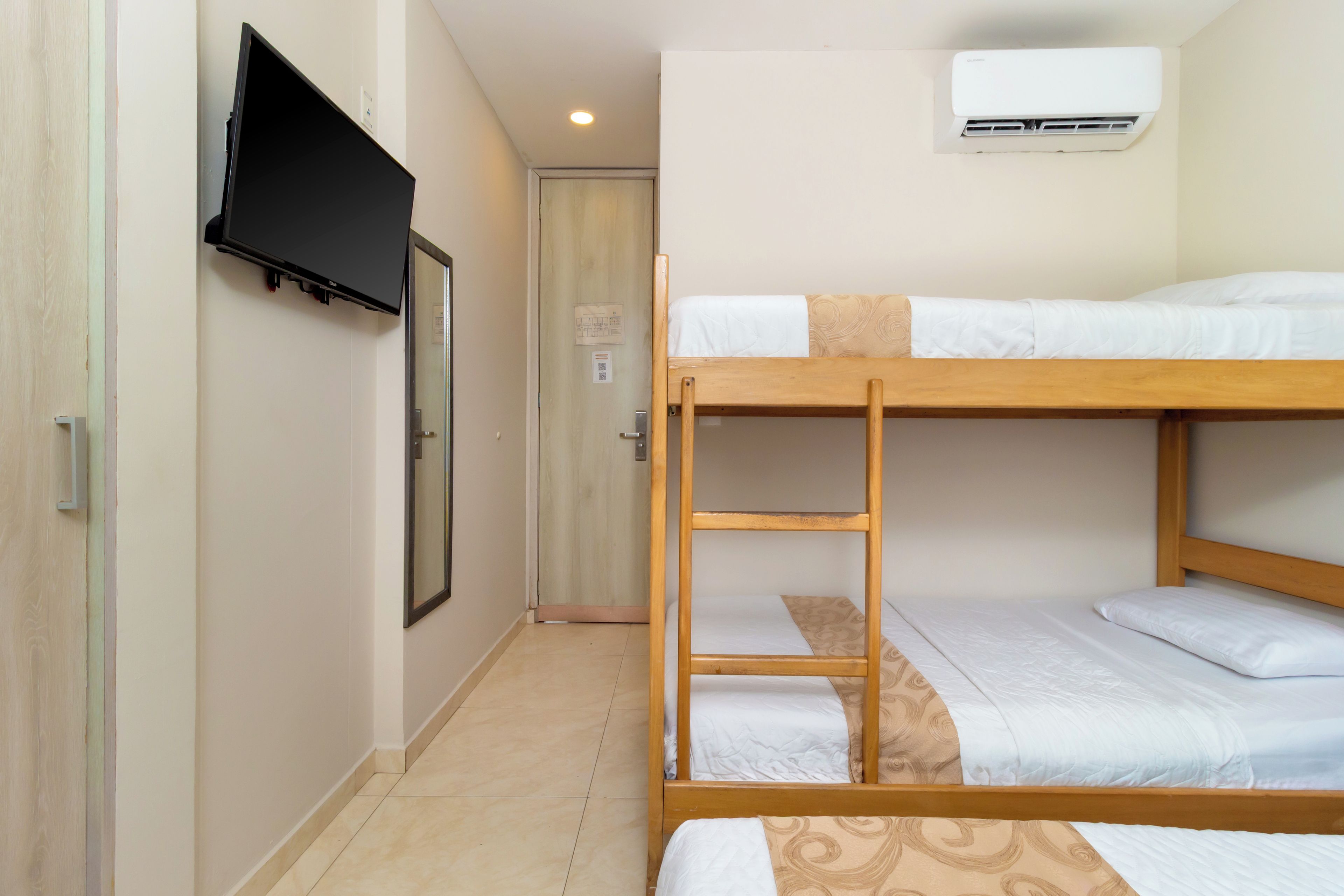 Une chambre avec des lits superposés, un téléviseur fixé au mur et un appareil de climatisation installé au-dessus.