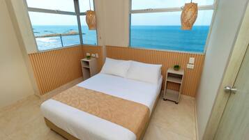 Un dormitorio con una cama grande, paneles de madera, dos mesitas de noche y vistas al mar a través de amplios ventanales.