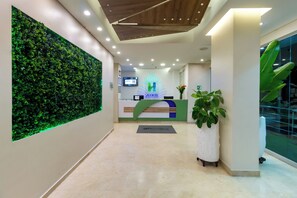 A hotel reception area with a green wall, a reception desk, a digital screen, and a potted plant. - Hotel Aixo Suites By Geh Suites (Cartagena)