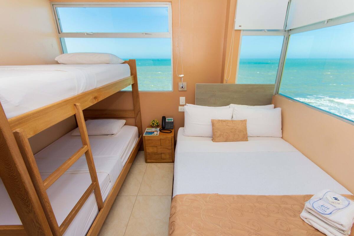 Una habitación con literas, una cama individual, una mesita de noche con teléfono y una ventana con vista al mar.