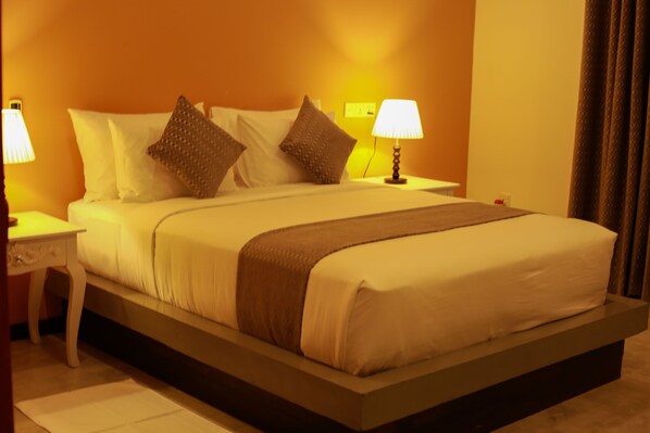Una cama bien hecha con sábanas blancas y dos almohadas marrones, una mesita de noche con una lámpara y un aplique de pared.