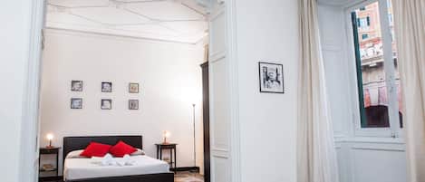 A bedroom with a bed, a nightstand, a framed picture, and a window with curtains.