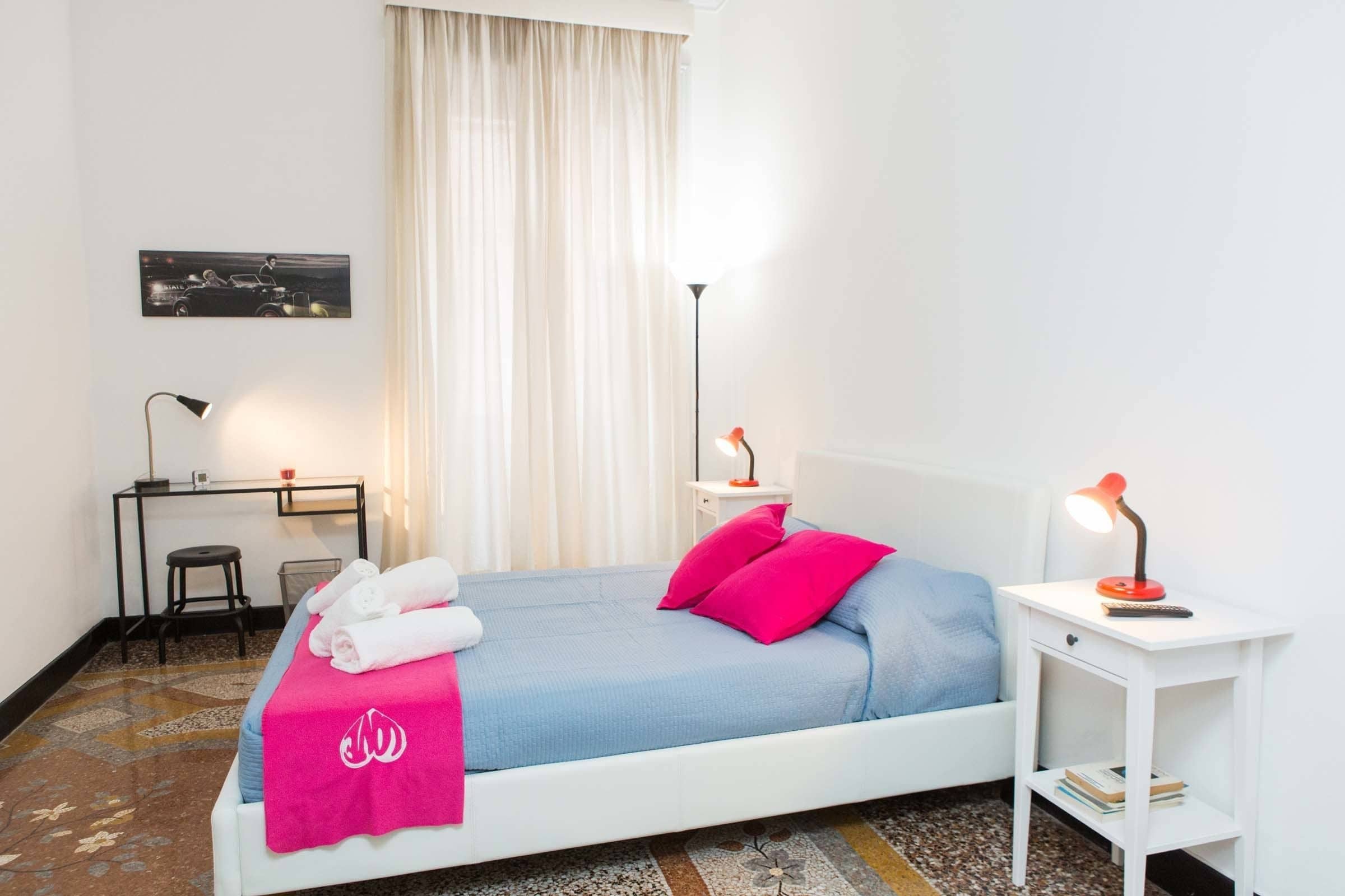 A neatly arranged bedroom with a bed, bedside tables, a desk, and a chair.