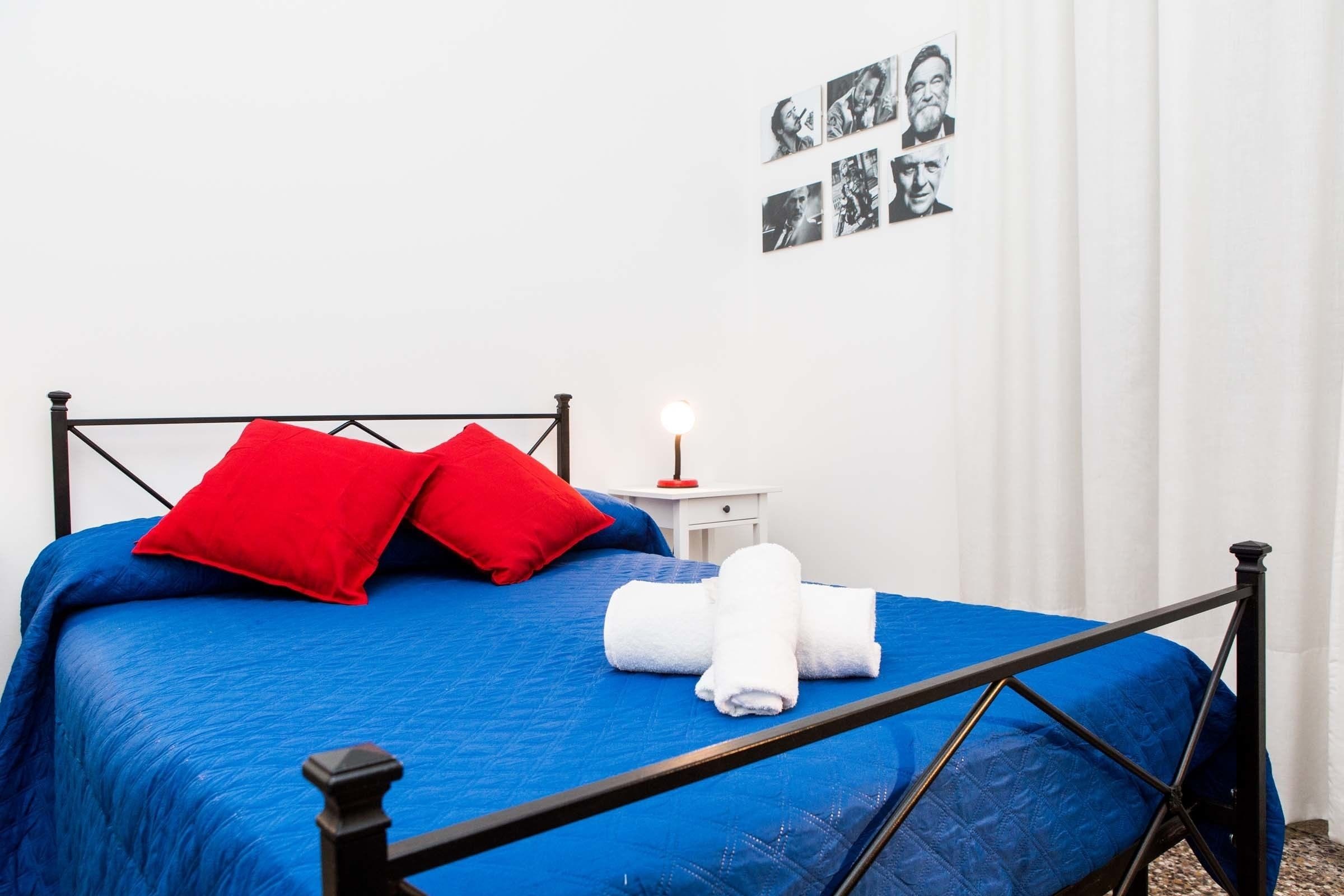A bed with a blue bedspread, two red pillows, and white towels.