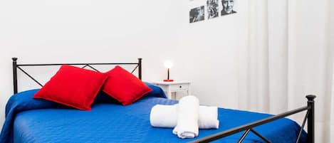 A bed with a blue bedspread, two red pillows, and white towels.