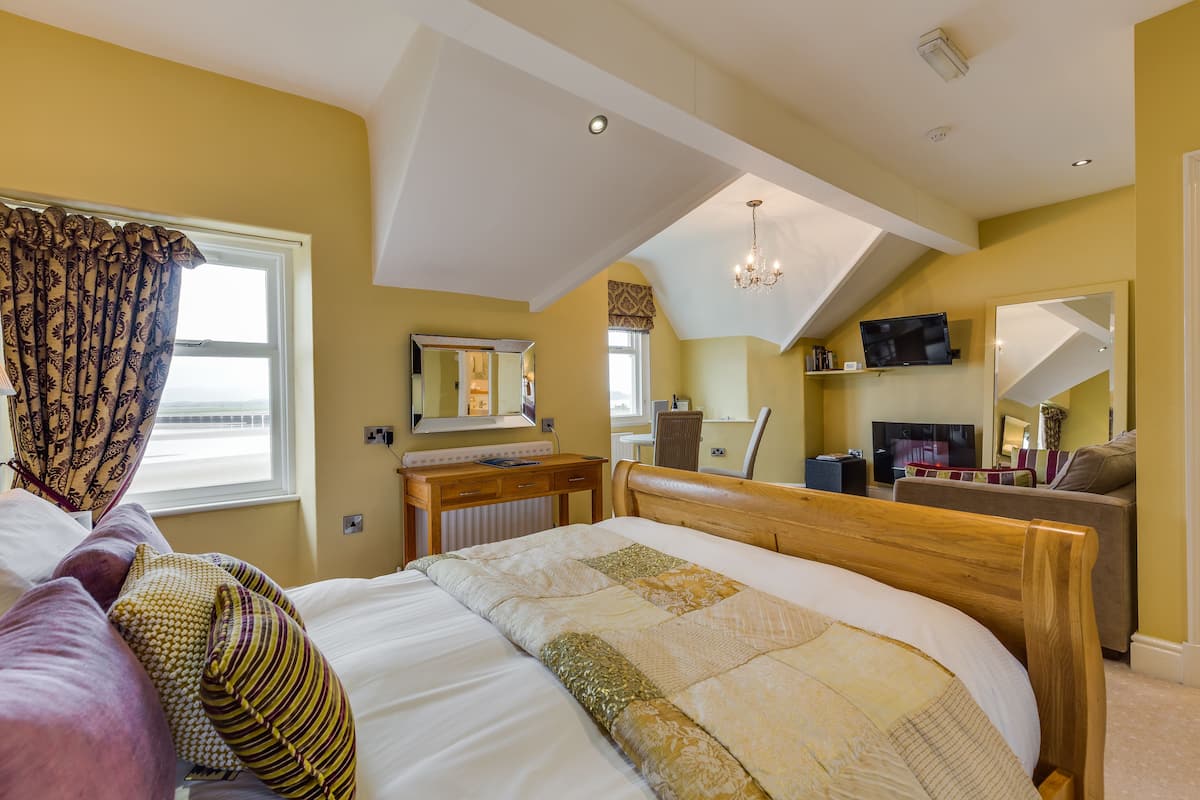 A bedroom with a large bed, a desk, a chair, a television, and a mirror.