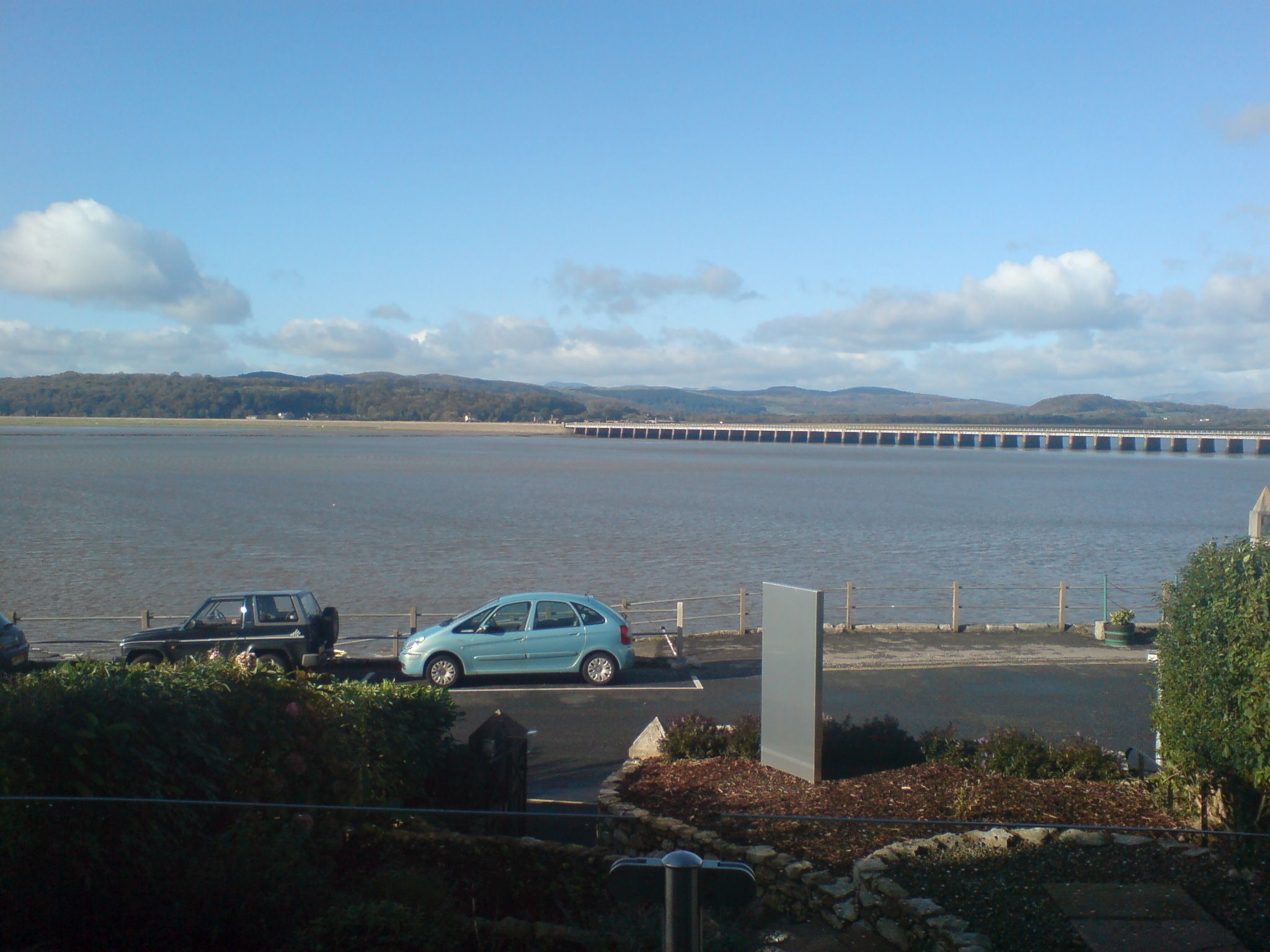 A parking area with a view of a bridge over water, surrounded by greenery.