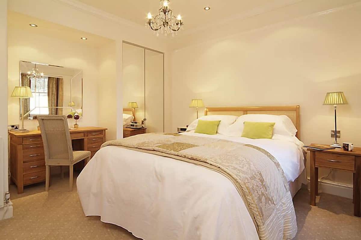 A bedroom with a large bed, a desk, a chair, and a mirror.