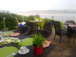An outdoor dining area with tables and chairs, a potted plant, and a view of a body of water.