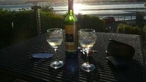 A table with two wine glasses and a bottle of wine, set against a scenic view of a river and distant hills. - Number 43 (Carnforth)