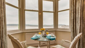 A corner room with a bay window overlooking the sea, a table set with breakfast, and two chairs. - Number 43 (Carnforth)