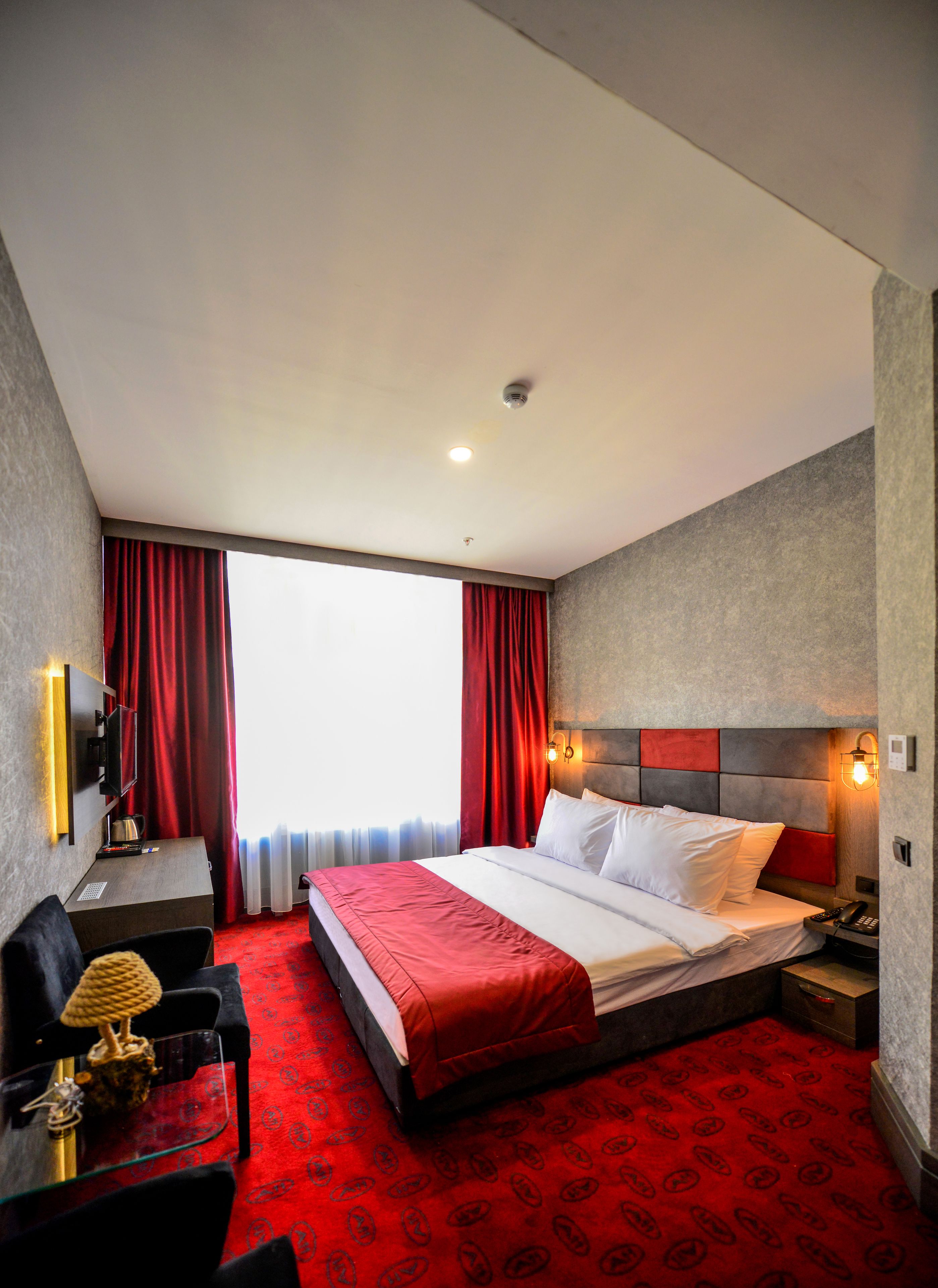 Ein Hotelzimmer mit einem großen Bett, einem Schreibtisch, einem Sessel, einem Fernseher und einem roten Teppich.