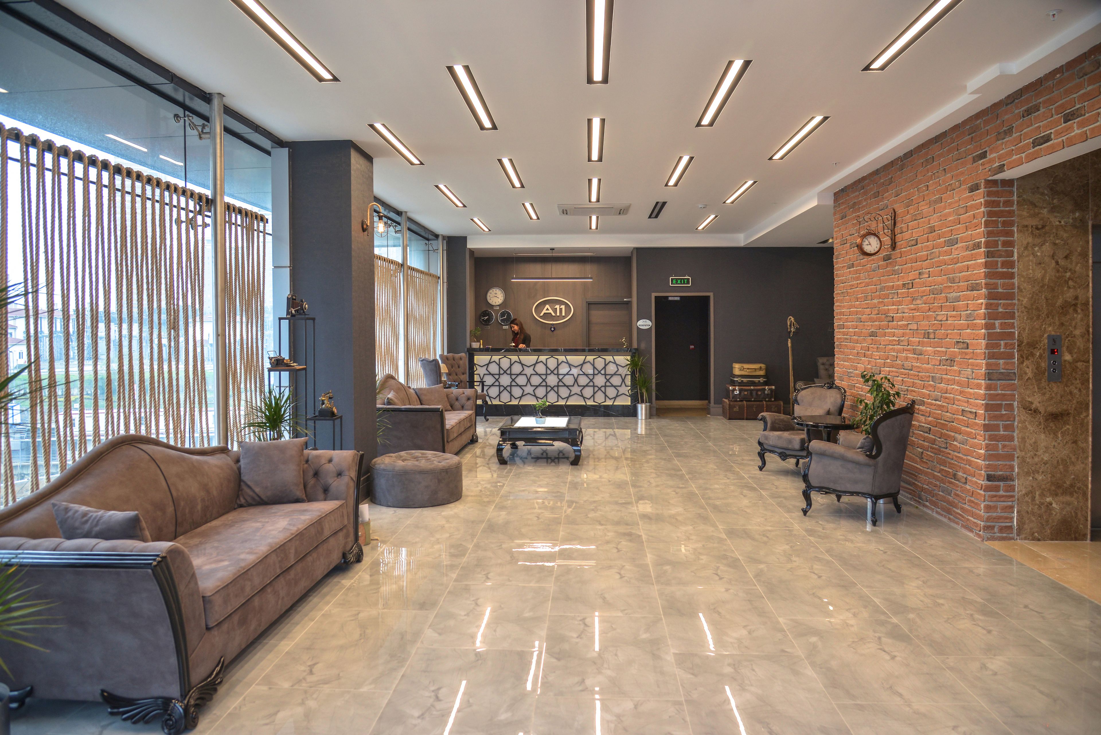 A spacious lobby with a modern design, featuring a leather sofa, armchairs, a coffee table, and a brick accent wall.