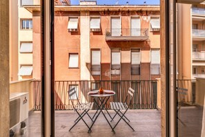 A balcony with a table and chairs, a view of a building with multiple windows and balconies, and a clear sky. - AwesHome - 5 Terre Colors (La Spezia)