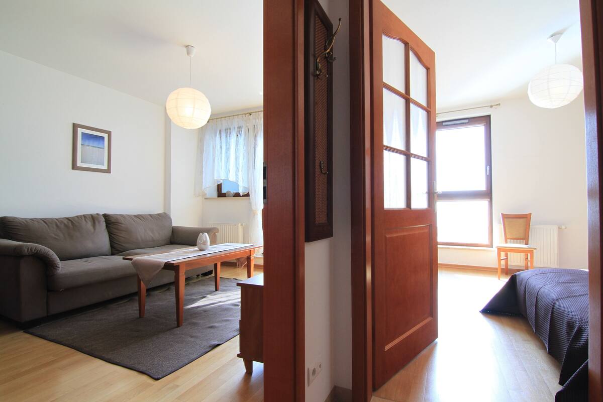 Un salon avec un canapé, une table basse et un tapis. Une porte donne accès à une autre pièce.