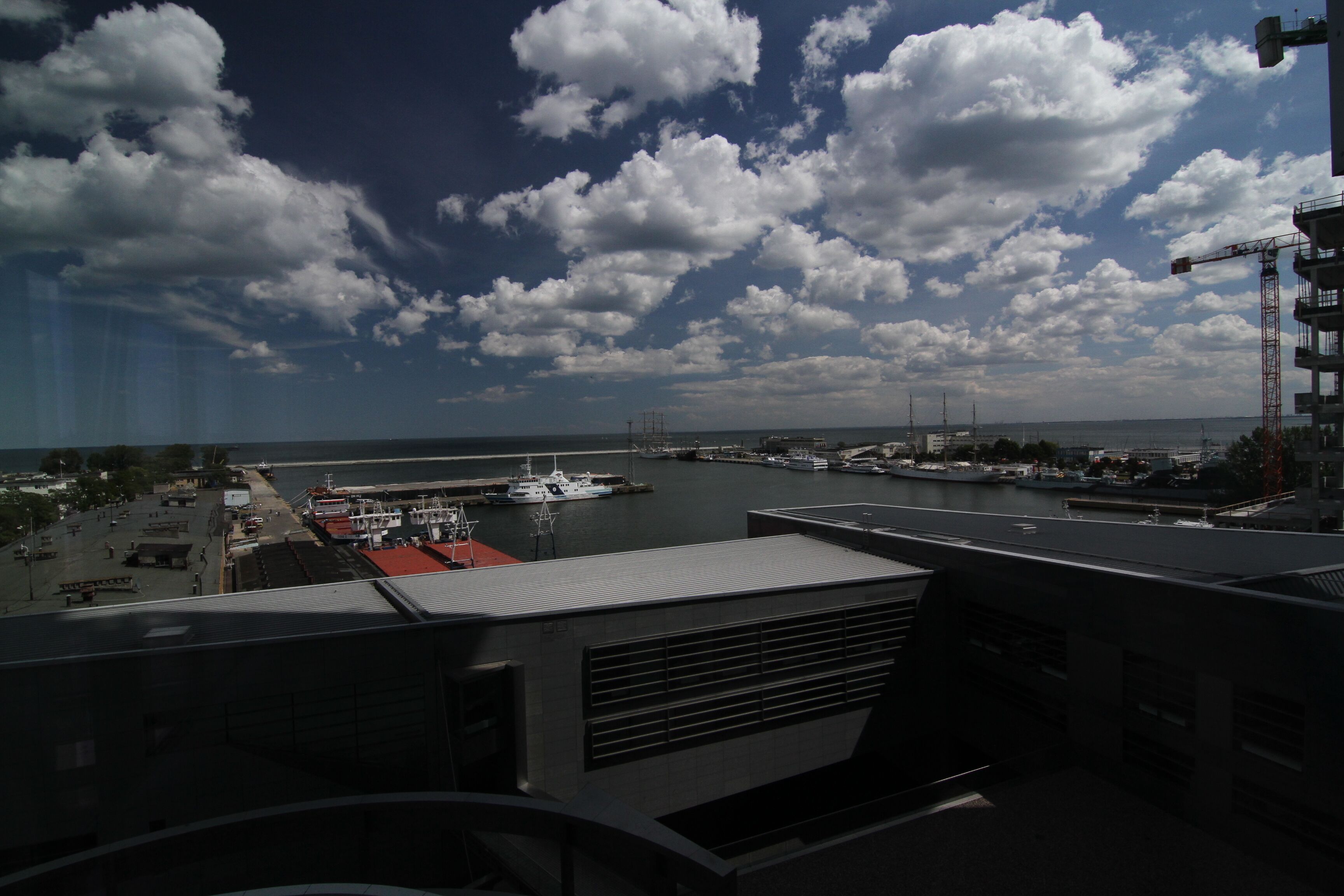 Vista desde un punto elevado sobre un puerto deportivo con barcos amarrados, cielo despejado con nubes dispersas y una costa lejana.