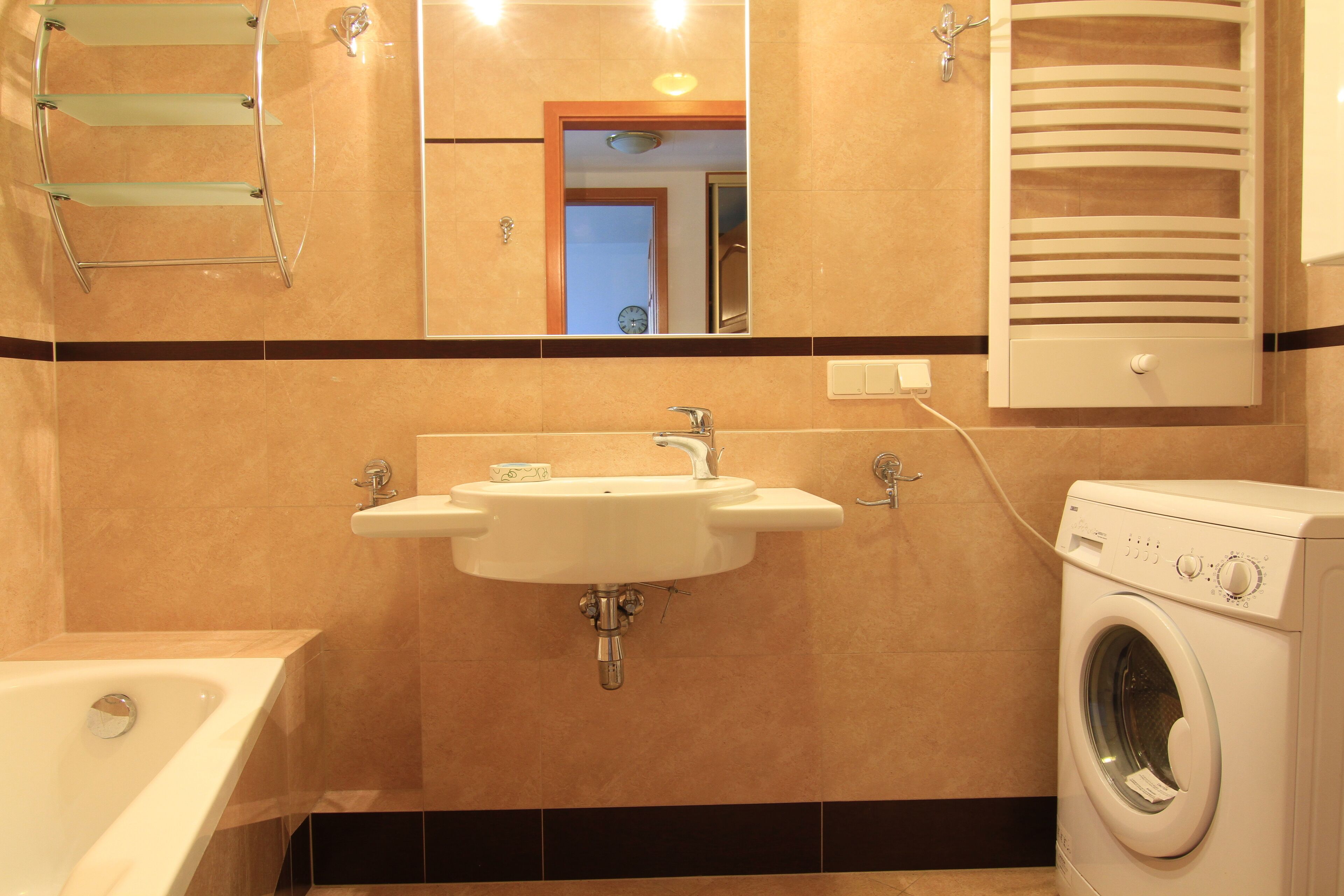 A bathroom with a sink, mirror, towel rack, and a washing machine.