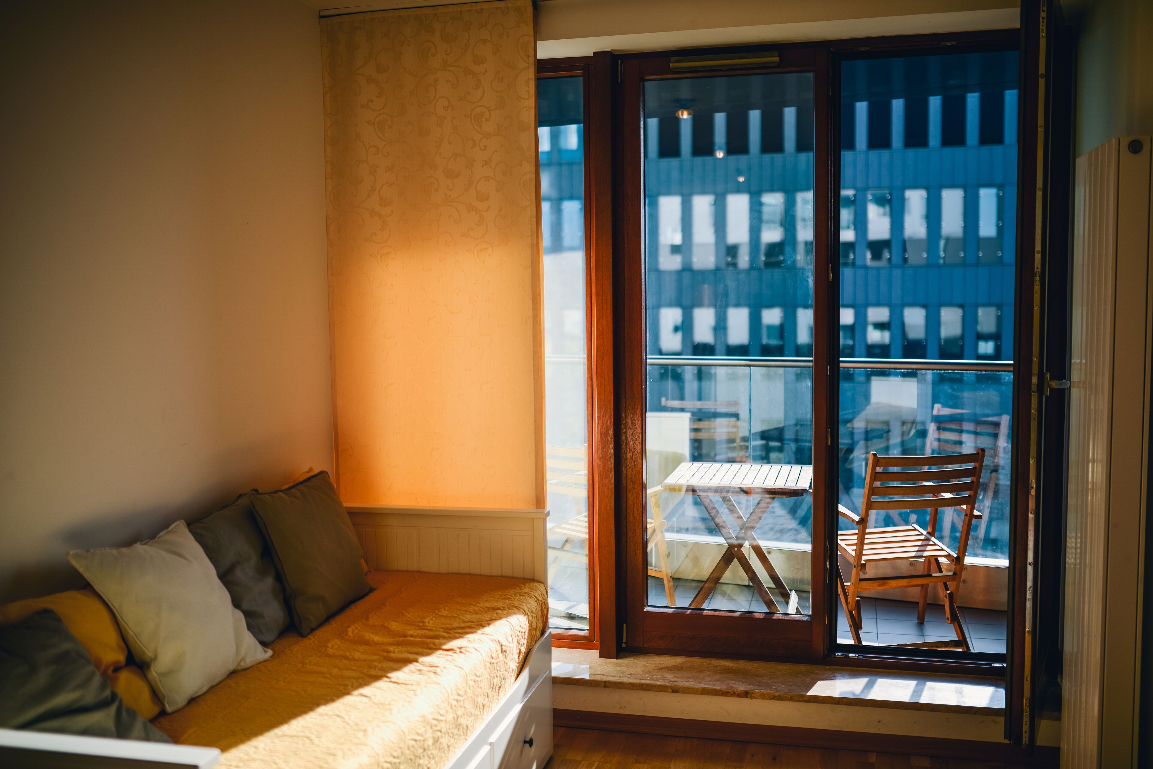 Une chambre à coucher avec un lit, une fenêtre et une vue sur un espace extérieur aménagé avec une table et des chaises.