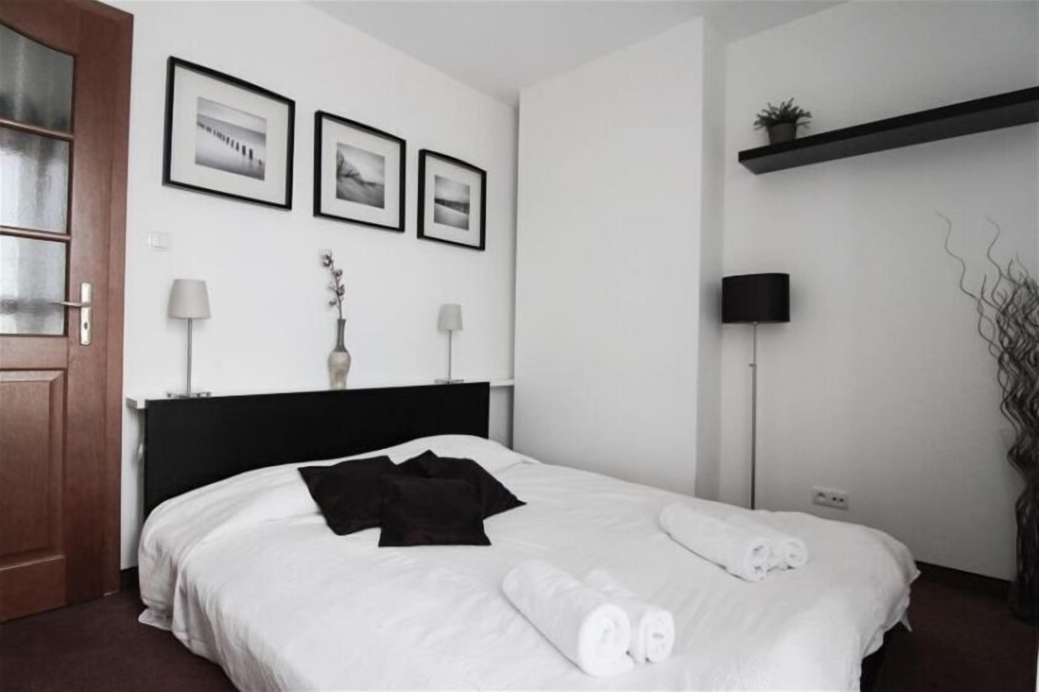 A hotel room with a bed, a nightstand, a lamp, a wall-mounted TV, and framed pictures on the wall.