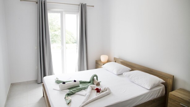 Una cama bien hecha con toallas y una toalla verde, una mesita de noche con una lámpara y una ventana con cortinas.