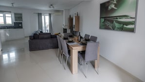 Un comedor moderno con una mesa de madera y sillas grises, un sofá gris y una cocina al fondo.