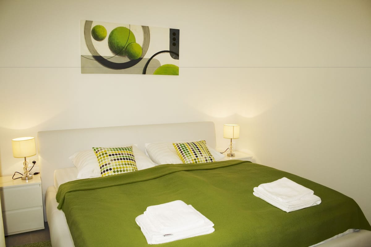 Ein ordentlich bezogenes Bett mit grüner Decke, weißen Kissen und gefalteten weißen Handtüchern.