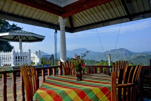A covered outdoor seating area with a table and chairs, a potted plant, and a view of mountains. - Cool Mount Resort (Ballaketuwa)