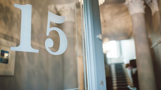 A close-up of a glass door with the number '15' on it, leading to a staircase with a chandelier in the background. - 15 Glasgow (Glasgow)