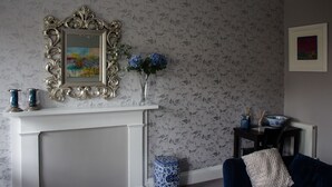 A room with a white fireplace, a floral wallpaper, a framed painting, a vase with flowers, and a blue and white bowl on a table. - 15 Glasgow (Glasgow)
