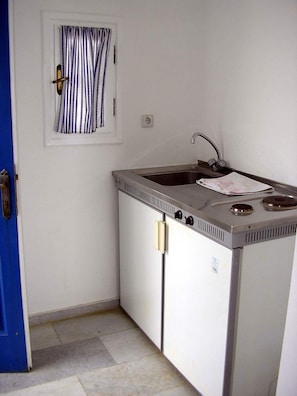 A compact kitchenette with a sink, stove, and a window with striped curtains.