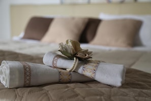 A neatly made bed with a beige quilt, a decorative pillow, and a rolled towel with a patterned border. - Maison Blanche (Pompei)