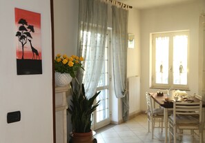 A dining area with a table and chairs, a potted plant, and a window with curtains. - Maison Blanche (Pompei)
