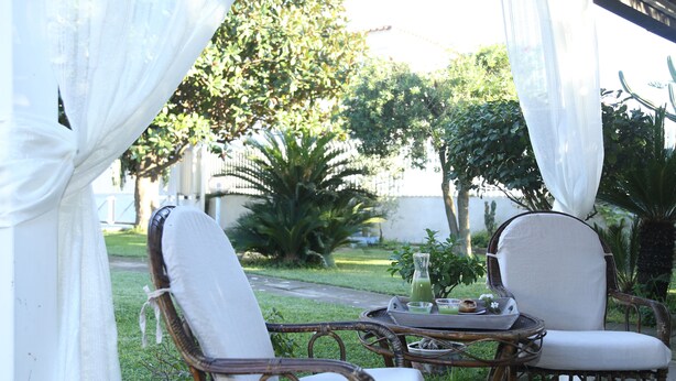 An outdoor seating area with wicker chairs and a table, surrounded by greenery and a white fence. - Maison Blanche (Pompei)