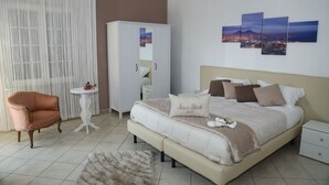 A bedroom with a large bed, a wardrobe, a chair, a small table, and a wall with three paintings. - Maison Blanche (Pompei)