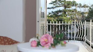 A balcony with a white railing, a small round table with flowers, and a view of trees and a fence. - Maison Blanche (Pompei)