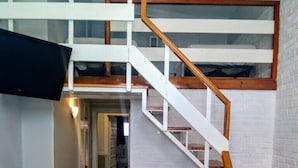 Une pièce de style « loft », avec un escalier en bois, des murs blancs et un sol carrelé.