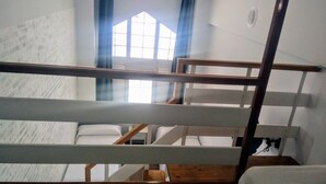 Une chambre de dortoir avec des lits superposés, une fenêtre avec des rideaux et un plancher en bois.